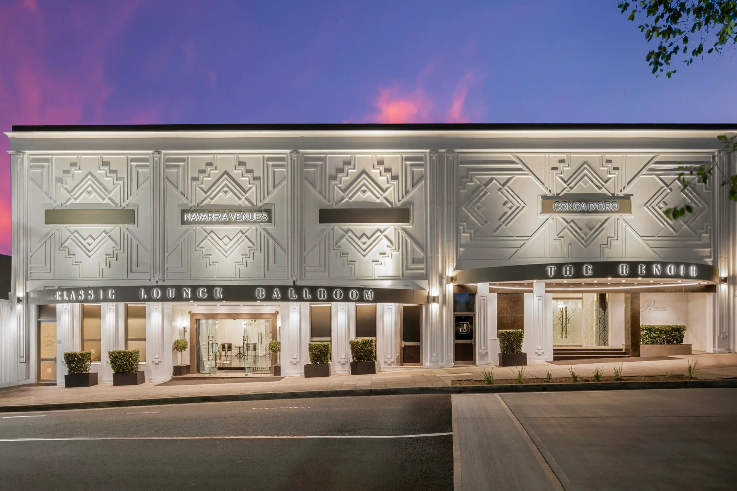 An Art Deco venue facade lit at dusk under a pink and violet sky